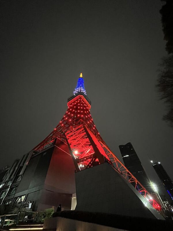 Der rot beleuchtete Tokyo Tower von unten fotografiert, die Spitze blau und gelb angestrahlt
